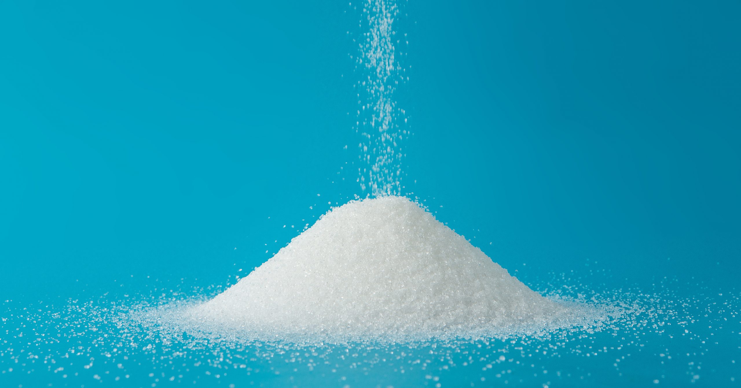 Heap of sugar with pouring on blue background